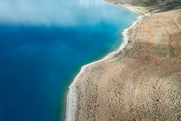 A stunning aerial view shows the contrast between dry, earthy terrain and the deep blue waters of a Tibetan lake.